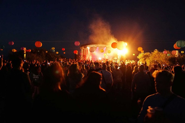 Eine Menschenmenge steht nachts vor einer Bühne, in der Luft schweben Ballons