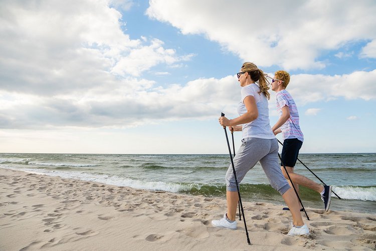 Eine Frau und ein junger Mann betreiben Nordic Walking am Strand