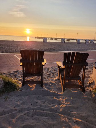 Zwei leere Holzsessel stehen bei Sonnenuntergang am Strand