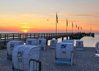 Ansicht der Seebrücke bei Dämmerung, im Vordergrund stehen weiße Strandkörbe