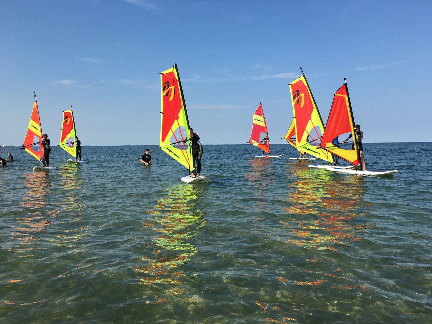 Eine Gruppe von Surfschülern mit rot-gelben Segeln lernt surfen