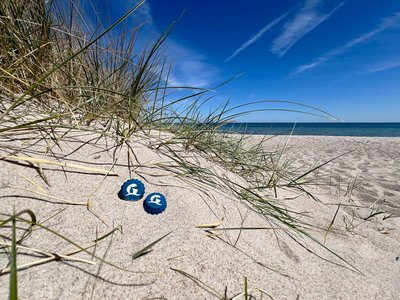 Zwei Silikonkorken liegen am Strand in einer Düne