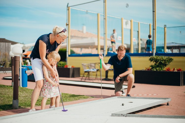 Ein Mutter bringt ihrer kleinen Tochter Minigolfspielen bei